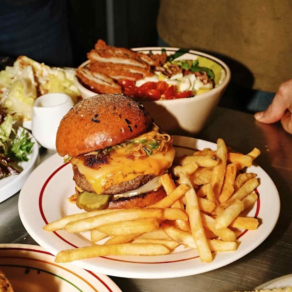 Cheeseburger with pickles, lettuce, and onions served alongside fries, salad, and a bowl of vegetables.